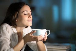 Relaxed woman smelling decaffeinated coffee in the night at home