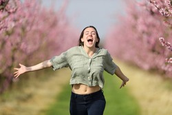 Front view of a happy woman running towards camera celebrating vacation in a pink flowered field in spring