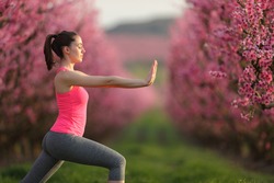 Side view portrait of a woman practicing tai chi exercise in a pink flowered field at sunset