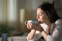 Relaxed woman smelling coffee in the morning sitting in the living room at home