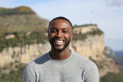Front view portrait of a happy man with black skin smiling at camera in the mountain