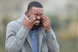 Stressed man with black skin scratching his eyes in winter