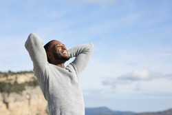 Relaxed man with black skin breathing fresh air with hands on head in the mountain