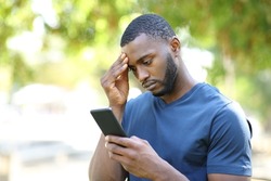 Worried man with black skin checking mobile phone standing in a park