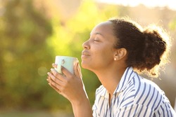 Profile of a relaxed black woman drinking coffee and smelling aroma in a park
