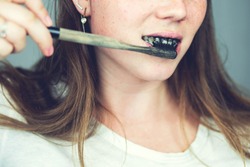 young woman brushing her teeth with a black tooth paste with active charcoal, and black tooth brush on white background for Teeth whitening clean