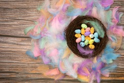 Colorful bright easter eggs in bird nest with Pastel colored feathers and wooden background texture top view, Copy Space, Spring, Easter Holliday, greeting card concept colorful design