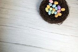Colorful Easter Egg Nest with Extra White or Gray Wood Board Background for room or space for copy, text, words. A flat lay with square crop, Happy Easter Holliday concept top view