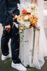 stylish couple, the groom in white sneakers, the bride holds a bright bouquet of seasons garden summer flowers, orange cosmos flowers, dahlia, chrysanthemum