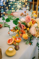 A large, long, decorated, wooden table and chairs, covered with a white tablecloth with dishes, flowers, candles, stands outdoor near the forest in nature. Wedding banquet. lights on background
