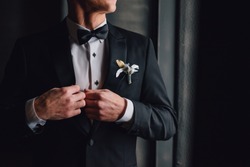 Groom in black tuxedo and bowtie correct his buttons on white shirt. Wedding. Details