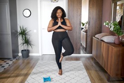 young african black woman keep balance, stand on one leg, yoga time at home. concentrated on yoga, meditation