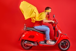 young crazy caucasian guy drive moped wearing cloak and mask rushing road party in super heroes role, isolated red color background