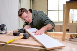 carpenter checking the wooden material, thinks if there are irregularities on it, wearing safety goggles for woodworking, looking seriously, concentrated on work. crafts, woodworking, carpentry
