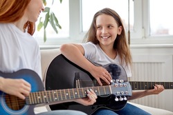 Learning to play the guitar. Nice Female teacher explains to child the basics of playing guitar in bright cozy room, at home. Individual home schooling or extracurricular lessons. Side view portrait