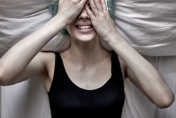 Upset depressed female is crying in tears lying on bed in bedroom. Attractive unhappy young woman feeling sad lonely and upset with life problem covering face with hands, at home
