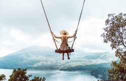Woman with hat enjoying freedom on a swing in Bali, Indonesia. Life, adventure and peaceful feelings