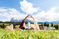Romantic couple in love doing picnic visiting mountains alps. Boyfriend and girlfriend enjoying love doing heart shape with hands outdoor.