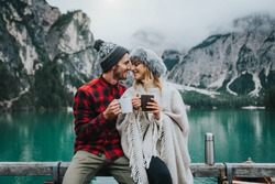Portrait of a romantic couple of adults visiting an alpine lake at Braies Italy at winter. Tourist in love drinking hot coffee at mountains. Couple, wanderlust and travel concept.