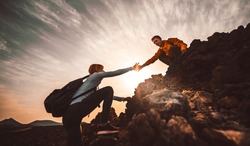 Couple of hikers helping each other climbing a mountain at sunset. People giving a helping hand and active sport concept.
