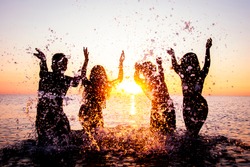 Happy friends splashing inside water on tropical beach at sunset  - Group of young people having fun on summer vacation - People, holidays and summertime concept