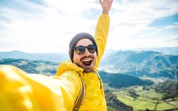 Young hiker man taking selfie portrait on the top of mountain - Happy guy smiling at camera - Hiking, sport, travel and technology concept - Bright filter