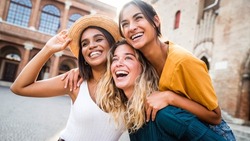 Three young multiracial women having fun on city street outdoors - Mixed race female friends enjoying a holiday day out together - Happy lifestyle, youth and young females concept