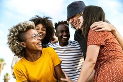 Happy multiracial friends laughing out loud together - Diverse young people having fun walking outdoors - Friendship concept with guys and girls socializing and joking outside