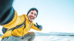 Young man wearing winter clothes taking selfie picture in winter snow mountain - Happy guy with backpack hiking outside - Recreation, sport and people concept