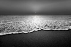 Wave and sandy beach in black and white. Calm view during sunset at seaside.