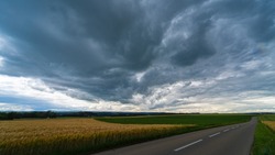 Stormy clouds, dramatic sky above rural farmland and asphalt road