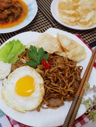 bakmi goreng jawa or fried noodles from java, served with slice cucumber, tomato, cabbage, and cucumber and crackers. gritty and grainy textured