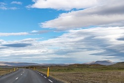 Panoramic view down a curving two lane road on Iceland, through barren Icelandic Highlands with volcanos and mountains in northern part of the country with beautiful blue sky with white fluffy clouds