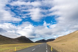 Panoramic view down a two lane road on Iceland, through barren Icelandic Highlands with volcanos and mountains in the northern part of the country with a beautiful blue sky with white fluffy clouds