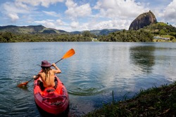 Young athletic man with dreadlocks and hat on a kayak on the lake. In the background the stone of Peñol, in Guatape Colombia