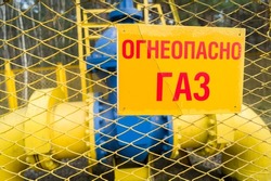 Russian text on warning sign - Flammable Gas. Blurred large shut-off mechanism on the gas supply pipe. Shut-off valve to stop the pumping of gas through the pipe line. Defocused