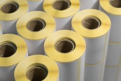 Rollers with a white self-adhesive label for printing labeling information. Ribbon with white label on cardboard spools. Products of the printing house. Selective focus