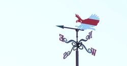 An eagle weather vane in the blue sky, on the wings of which is a white-red-white flag