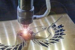 A laser engraving machine cuts out a picture on a gold glossy plastic plate. Closeup