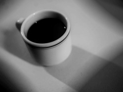 Black and white high angle view of a white coffee cup, with off-center square vignetting 