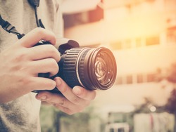 Photography or traveler Concept.The photographer hold DSRL camera in his hands with cityscape blur background and sunlight in summer time, selective focus. Photo of Vintage and filtered process.
