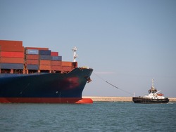 Large Container Ship Towed into Port by a Small Tugboat.