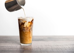 Ice coffee latte with cream being poured into it showing the texture and refreshing look of the drink, with a clean background.