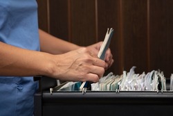Hands of health personnel reviewing files in the filing cabinet of the dental office.
