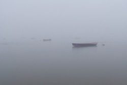 Misty morning on the river. Fishing boats fading in the mist. Fog covering river. Disappearing rowboat in the mist. Zemun coast in the misty morning