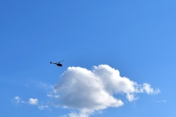 small silhouette of helicopter against big white cloud on blue sky