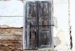 Dilapidated wooden window shutters of old abandoned house on white wall