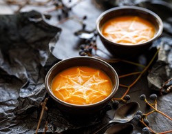 Halloween pumpkin soup with creamy spider web in black bowls on a dark background close up view