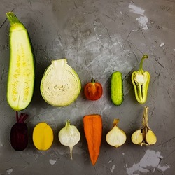 zucchini, cabbage, tomato, cucumber, pepper, carrot, beetroot, potato, radish, onion, garlic on a gray concrete background autumn vegetables in the section 