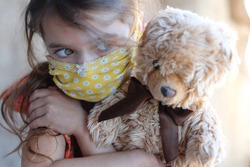 Masked Child with Favorite Doll Teddy Bears. Portrait Sad Little Girl. Serious Baby. Protective Mask. Preventive measures against covid-19, viruses, flu. Basic hygiene rules. Pandemic. Stay at Home
